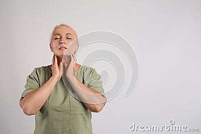 Mature woman doing thyroid self examination on light grey background, space for text Stock Photo