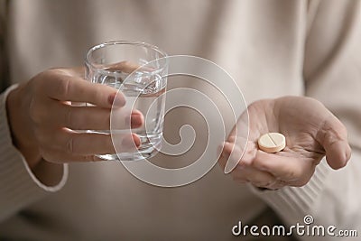 Mature woman holding glass of fresh water and round pill. Stock Photo