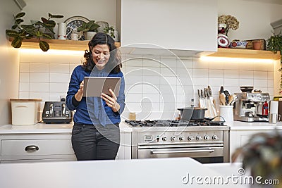 Mature Woman At Home In Kitchen Looking At Digital Tablet Stock Photo