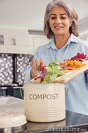 Mature Woman In Kitchen Making Compost Scraping Vegetable Leftovers Into Bin Stock Photo