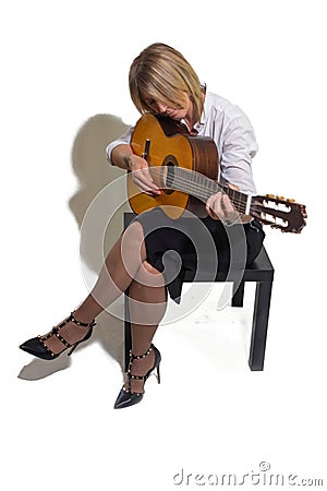 Mature woman sitting on a coffee table playing a musical instrument, the guitar. Stock Photo
