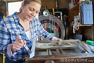 Mature Woman Upcycling Furniture In Workshop At Home Painting Cabinet Stock Photo