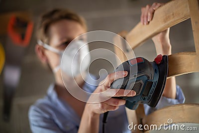 Mature Woman Upcycling Furniture In Workshop At Home Using Electric Sander Stock Photo