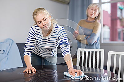 Mature woman watches as her daughter wipes the table Stock Photo