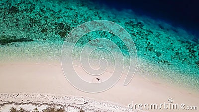 Maumere - A drone shot of a couple sitting on a white sand beach Stock Photo