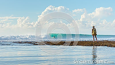 May 5 2019 : Balangan Beach, Bali, Indonesia - A woman watching as a surfer rides a nice wave with afternoon sun lighting the Editorial Stock Photo