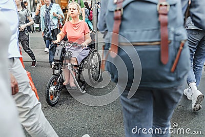 Senior woman on a disability scooter bike or wheelchair crossing busy city street with crowds of Editorial Stock Photo