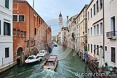 Water taxi crossing picturesque canal surrounded by vintage buildings, with bridge and bell tower in the distance Editorial Stock Photo