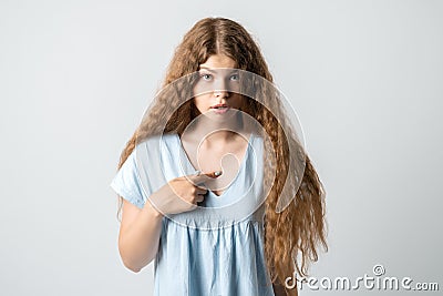 Me?! Portrait of indignant girl with curly long hair startled by offensive words, points at herself with for finger Stock Photo