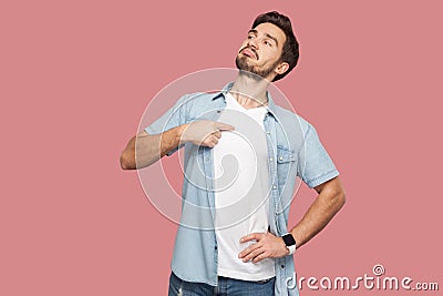 This is me. Portrait of proud haughty handsome bearded young man in blue casual style shirt standing, looking away and pointing Stock Photo