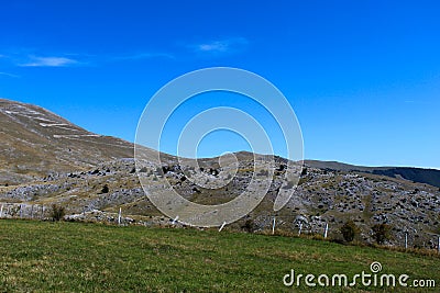 A meadow with a downed fence at the end of the meadow. In the background, mountain desolation, with little vegetation. Mountain Stock Photo