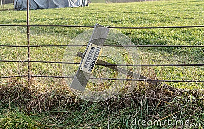 meadow with fence and a tipped over sign showing the german words 