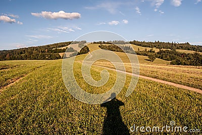 Meadow with pathway, photographer shadow, hill on the background and blue sky with clouds Stock Photo