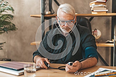 Measure your blood pressure. A retired man at home at the table monitors himself with a tonometer Stock Photo