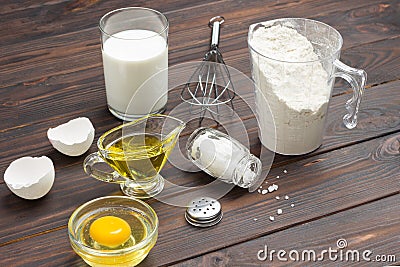 Measuring cup with flour, glass of milk, broken egg and salt, metal whisk on table Stock Photo