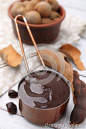 Measuring cup with tasty tamarind sauce and fresh pods on white wooden table Stock Photo