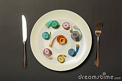 Measuring tape in a plate with fork and knife on both sides on black background. Top view of weight loss concept Stock Photo