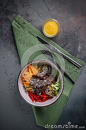 Meat salad with Beef Tenderloin, vegetables, orange, sesame seeds and herbs on a plate top view. Spoon and fork on a green Stock Photo