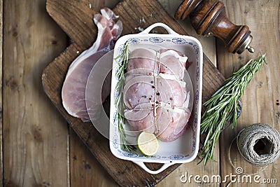 Meat tied with rope, on a baking sheet with lime and rosemary, on a wooden table and towel. Stock Photo