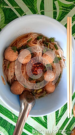 Meatball noodles with small white strips Served with garnish and vegetables. There are eating utensils, chopsticks and spoons. Stock Photo