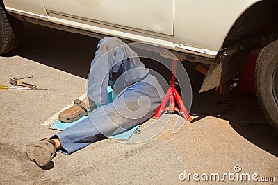 Mechanic in blue dirty uniform lying down and working under car at auto service garage Stock Photo