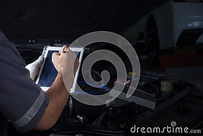 The mechanic checks the engine using tablet computer technology. Complete with wrench tool Auto mechanic working in the garage. Stock Photo