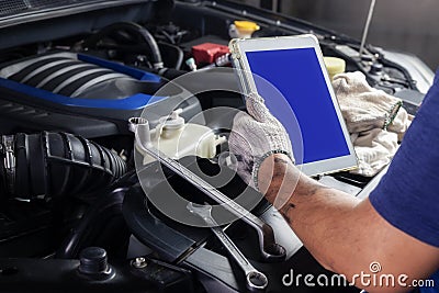 The mechanic checks the engine using tablet computer technology. Complete with wrench tool Auto mechanic working in the garage. Stock Photo
