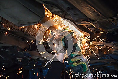 Mechanic cuts old muffler on car by angle grinder Stock Photo