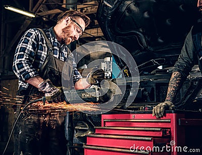 Mechanic cuts steel car part with an angle grinder. Stock Photo