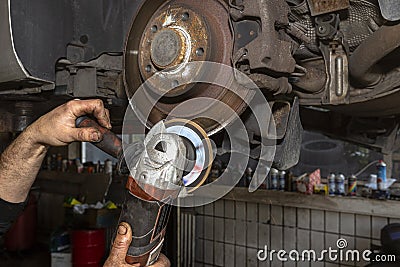 A mechanic grinds, with an angle grinder, the edge of an old rear brake disc in a car, regeneration of the brake system. Stock Photo