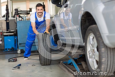 Mechanic hands in blue uniform pushing a black tyre Stock Photo