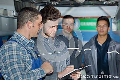 mechanic and male trainee working underneath car together Stock Photo