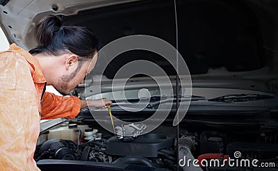 The mechanic in an orange dress uniform opened the car bonnet and discovered an abnormality preventing the car to start. The Stock Photo