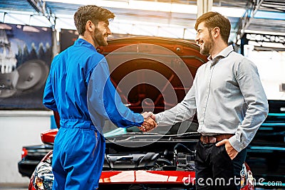 The mechanic shaking hands with customer after finish checking the opened hood red car. Happy mechanic and satisfied customer. Stock Photo