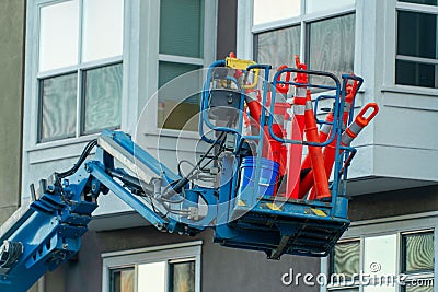 Mechanical crane or cherry picker filled with orange reflective traffic cones in an dense urban setting in afternoon shade Stock Photo