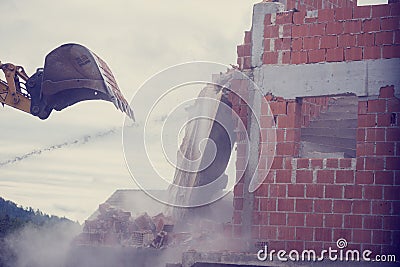 Mechanical digger demolishing the wall of a brick building Stock Photo