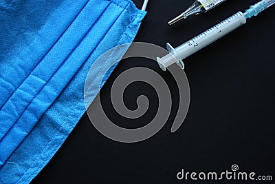 Medical backdrop with a face mask, thermometer and plastic syringe. Black background. Close up. Template Stock Photo