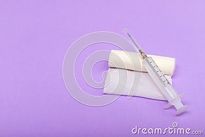 Medical bandage and syringe on a lilac background. A gauze roll on which the syringe lies. Dressing for medical purposes. Space Stock Photo