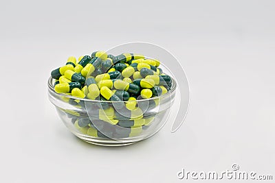 Medical capsules yellow green in glass bowl closeup against white Stock Photo