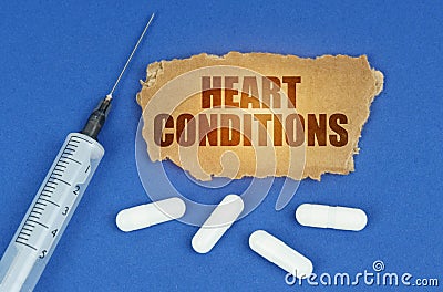 On a blue surface lie a syringe, pills and a cardboard sign with the inscription - HEART CONDITIONS Stock Photo