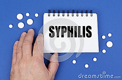 On the blue surface of the tablet, a hand and a notepad with the inscription - SYPHILIS Stock Photo