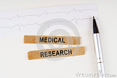 On the cardiogram lies a pen and torn paper with the text - MEDICAL RESEARCH Stock Photo