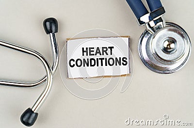 On a gray background, a stethoscope and a cardboard sign with the inscription - HEART CONDITIONS Stock Photo