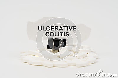 On a white surface are pills and torn paper with the inscription - ULCERATIVE COLITIS Stock Photo