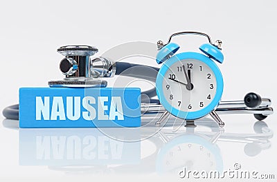 On a white surface there is an alarm clock, a stethoscope and a blue block with the inscription - NAUSEA Stock Photo