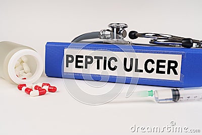 On a white surface there are pills, a syringe and a folder with the inscription - Peptic ulcer Stock Photo