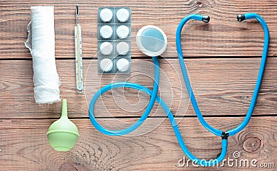 Medical equipment of the therapist on a wooden table: stethoscope, enema, thermometer, tablets, bandage. Top view. Stock Photo