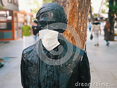 Medical face mask attached to the face of a statue on the street Stock Photo