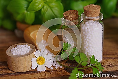 Medical glas vials on wooden table, filled with globulis. Decoratet with leaves and flowers. Homeopathy conzept. Stock Photo