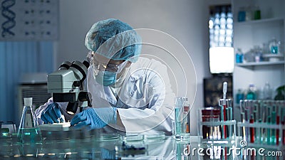 Medical lab worker examining laboratory glass with sample through microscope Stock Photo